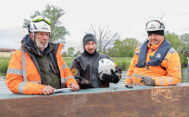 Slide Taucher und Experten von Lutomsky zeigen ein Fundstück vom letzten Tauchgang. 